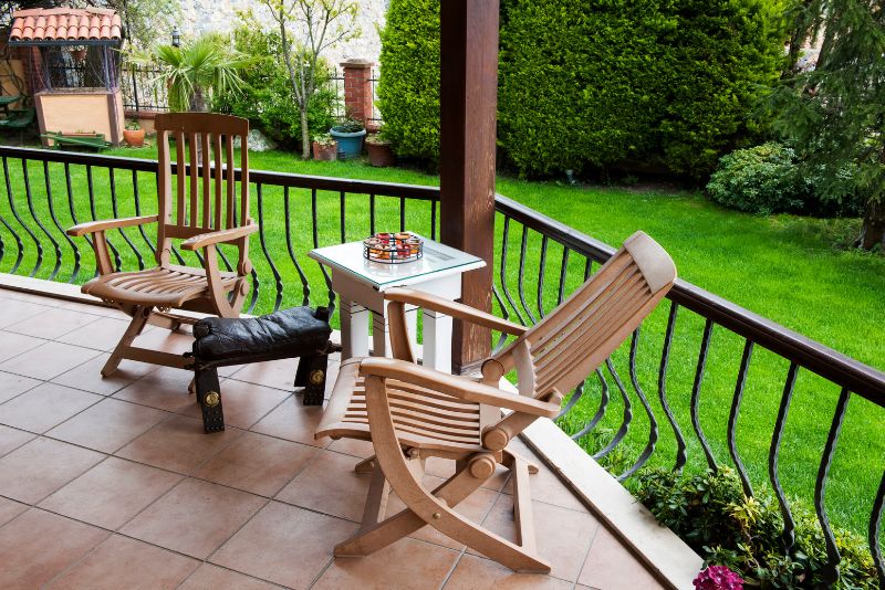 patio with a small table and two chairs with a railing and plants and freshly trimmed lawn round